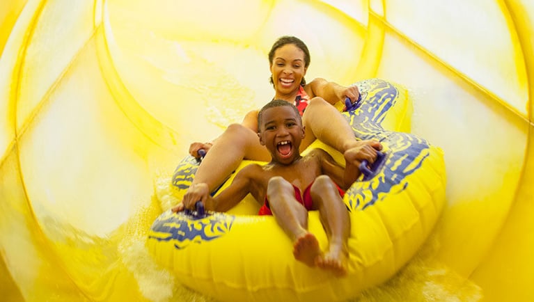 Mother and son in a tube racing down a yellow waterslide 